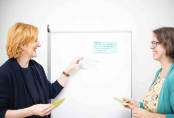 Marie steht bei einem Flipchart mit einer Kundin.